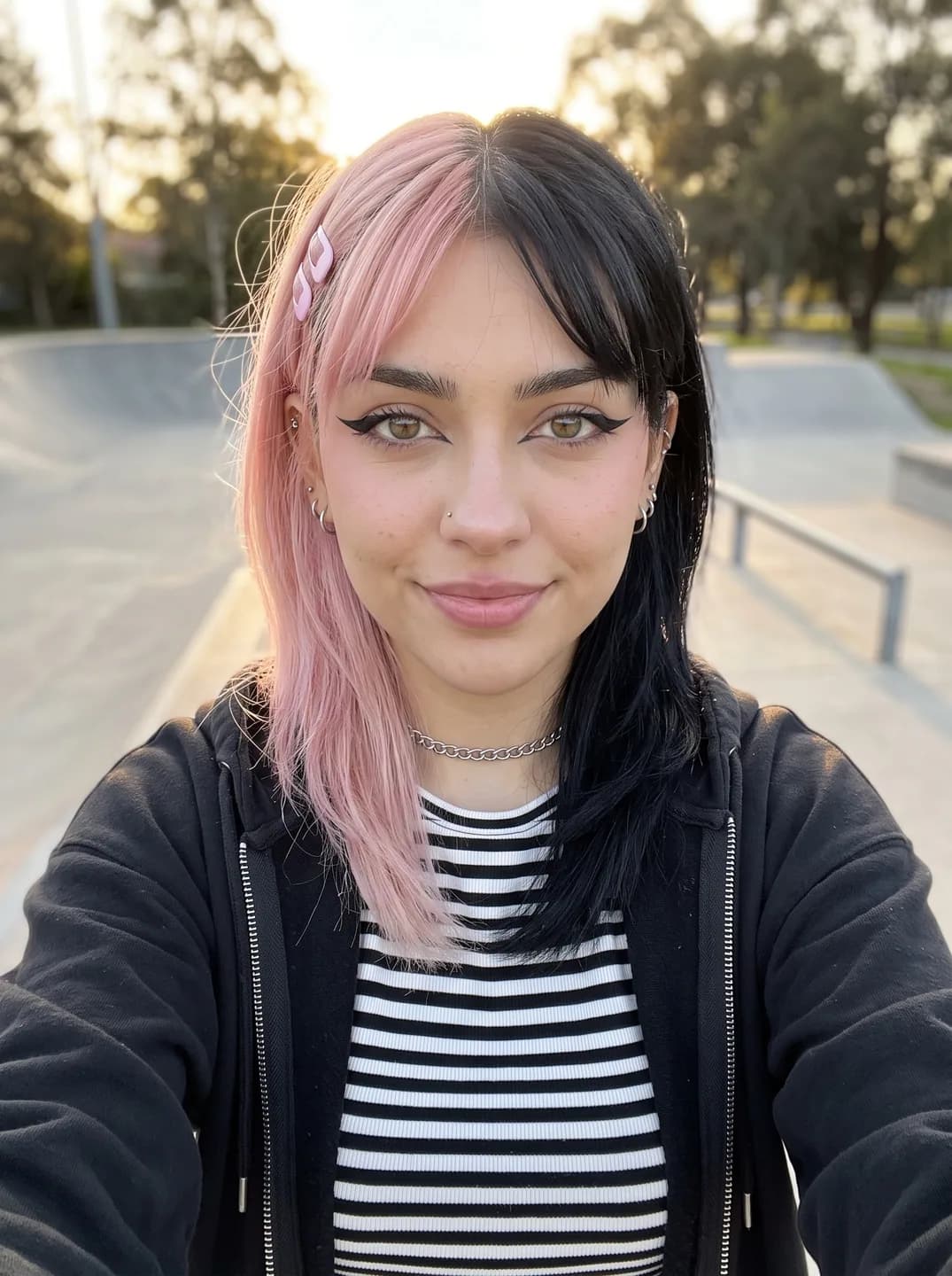 AI-generated sample input: front-facing selfie of a woman with split pink and black hair and winged eyeliner in a black zip hoodie over a striped top at a skatepark