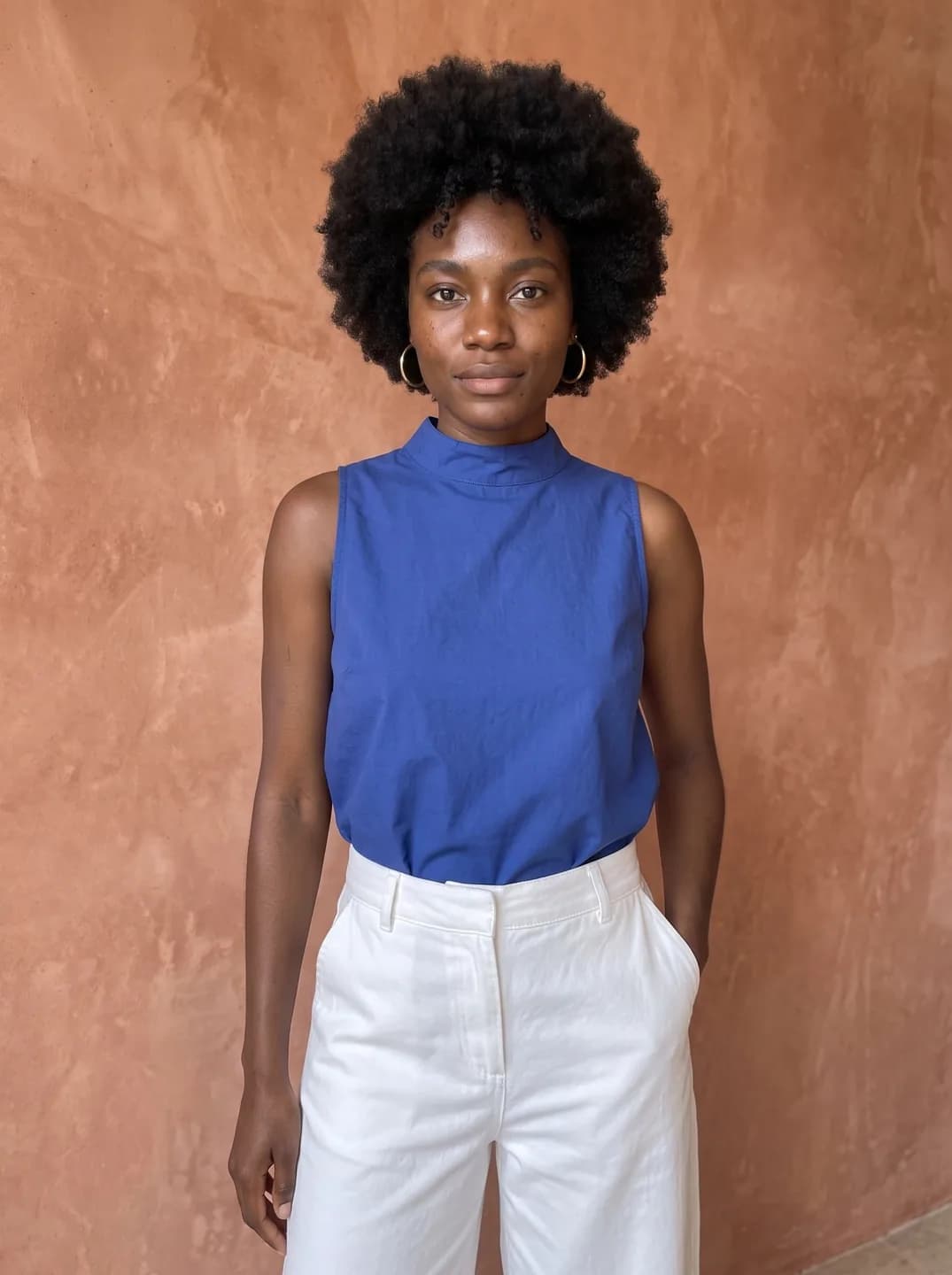 AI-generated sample input: waist-up photo of a woman with a natural afro in a sleeveless cobalt blue top and white trousers against a terracotta wall