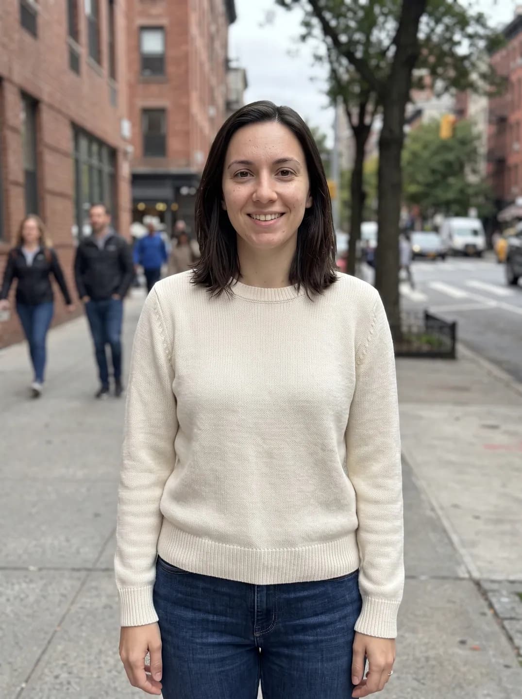 AI-generated sample input: waist-up photo of a woman with shoulder-length dark brown hair in a cream sweater and jeans on a city sidewalk