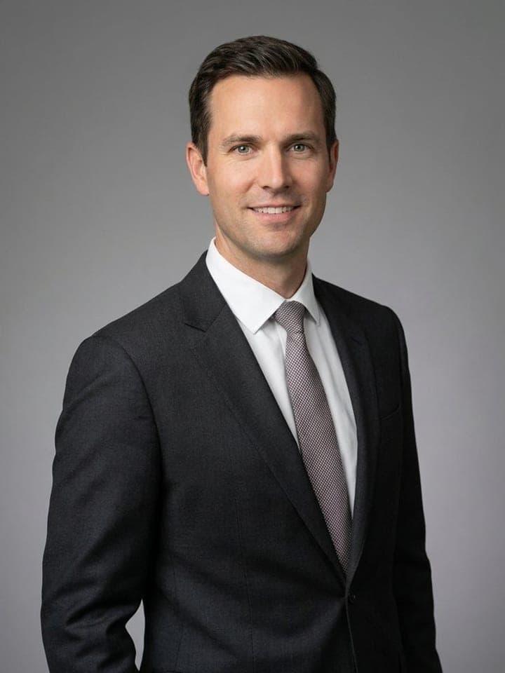Man in a dark suit and tie smiling in a professional headshot on a grey studio background