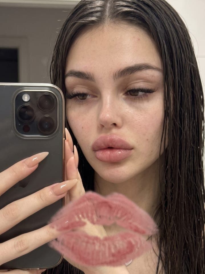 Mirror selfie of a woman with wet hair holding an iPhone, a pink lipstick kiss print on the glass