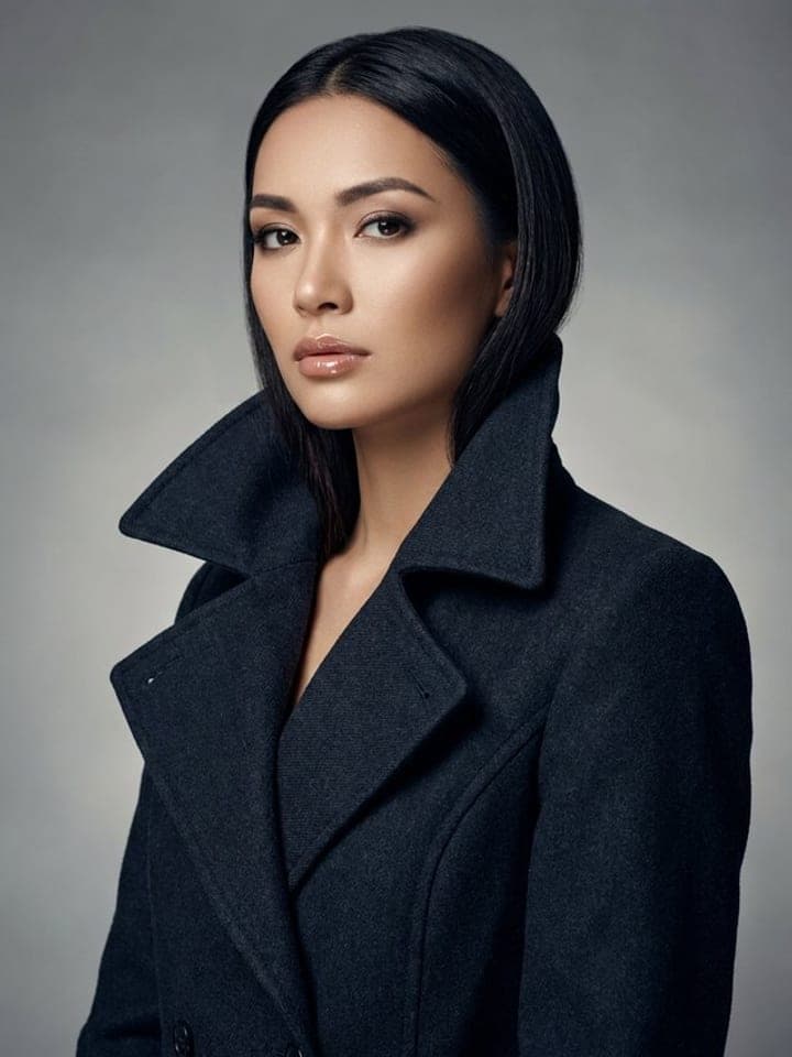Editorial cover portrait of a woman with sleek black hair in a black wool coat on a grey studio backdrop