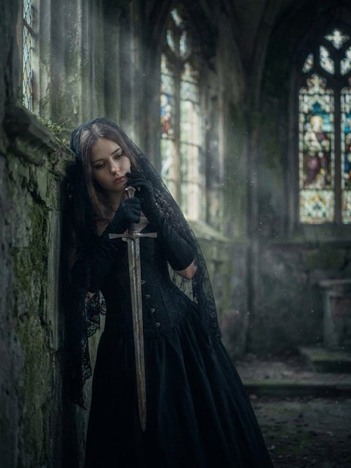 Woman in a black corset dress and lace veil holding a sword in the ruins of a gothic cathedral