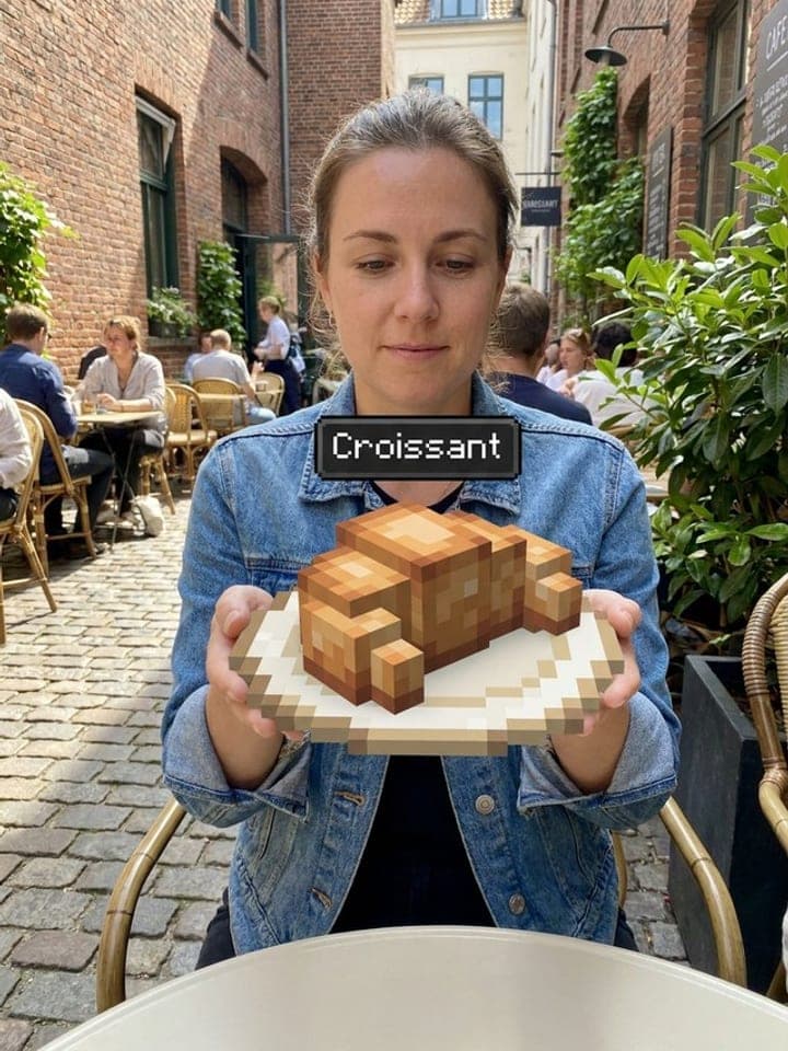 Woman at a street cafe holding a plate with a blocky Minecraft-style croissant and a Croissant tooltip