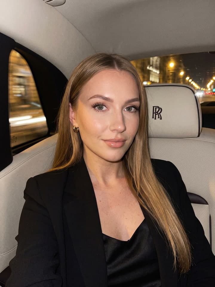 Frau mit langen blonden Haaren macht nachts ein Selfie auf der Rückbank eines Rolls-Royce, RR-Monogramm auf der cremefarbenen Kopfstütze