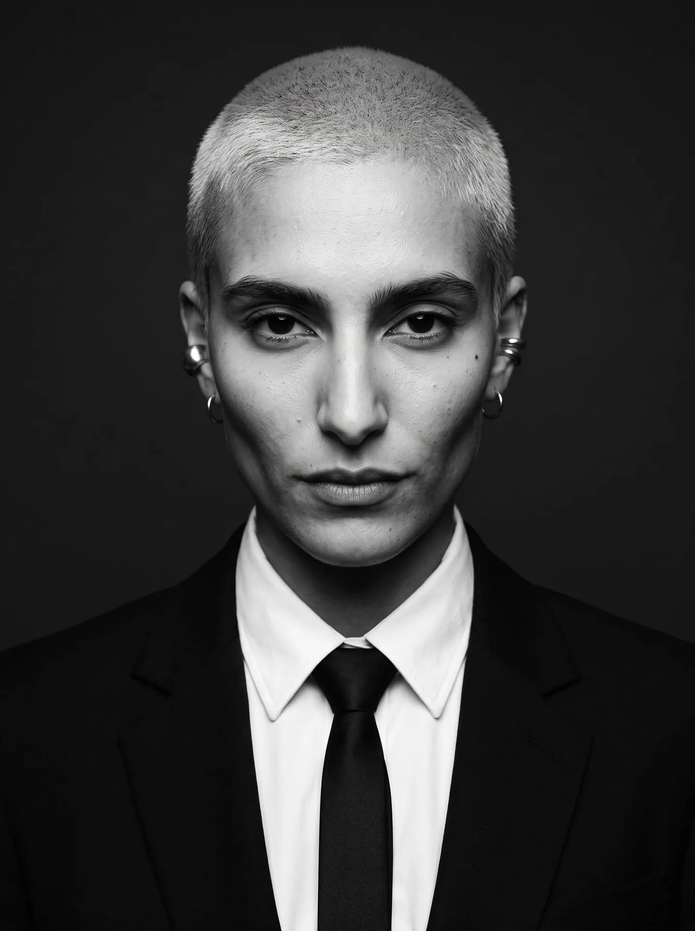 Black-and-white portrait of a woman with a buzz cut in a black suit, white shirt and slim black tie