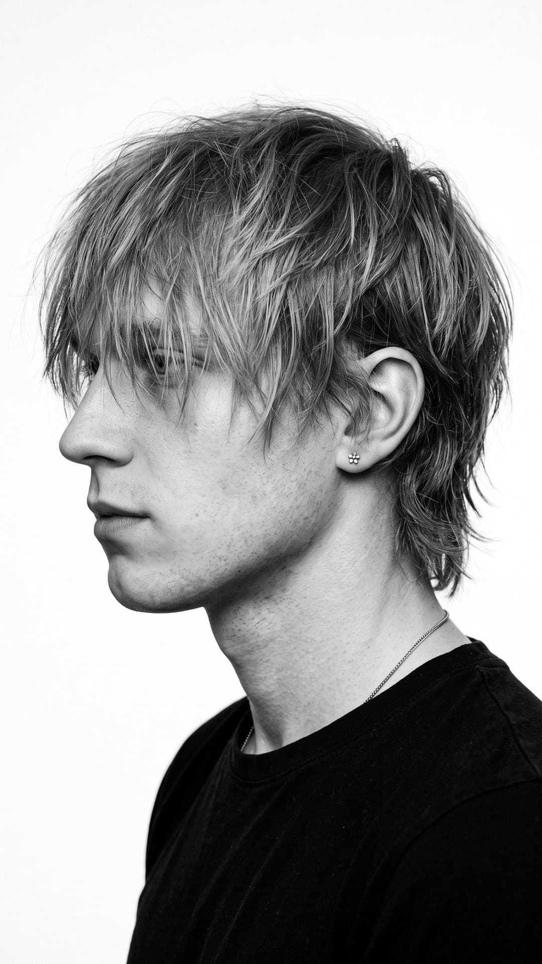 Schwarz-Weiß-Seitenprofil eines jungen Mannes mit langen zotteligen blonden Haaren über dem Auge, schwarzes T-Shirt, weißer Hintergrund