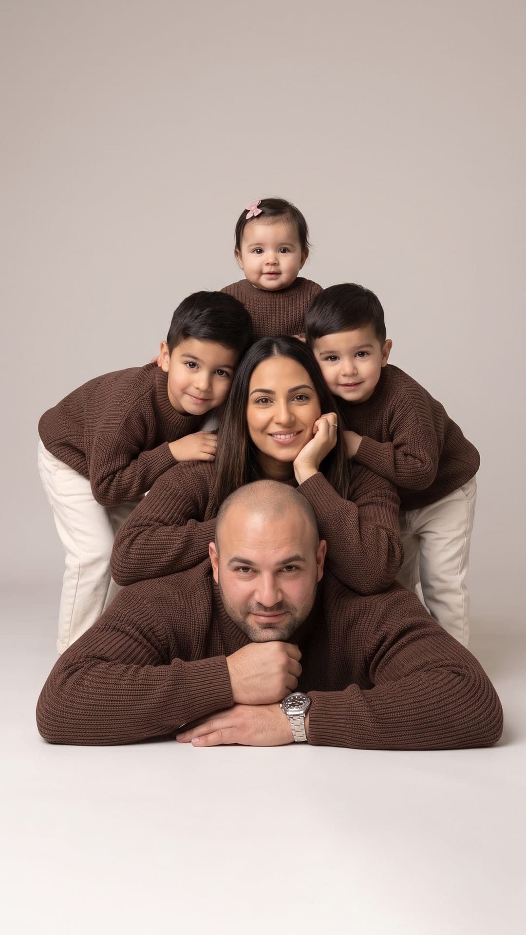 Familienpyramide im Studio aus Papa, Mama, zwei kleinen Jungen und einem kleinen Mädchen in passenden braunen Strickpullis vor hellgrauem Hintergrund