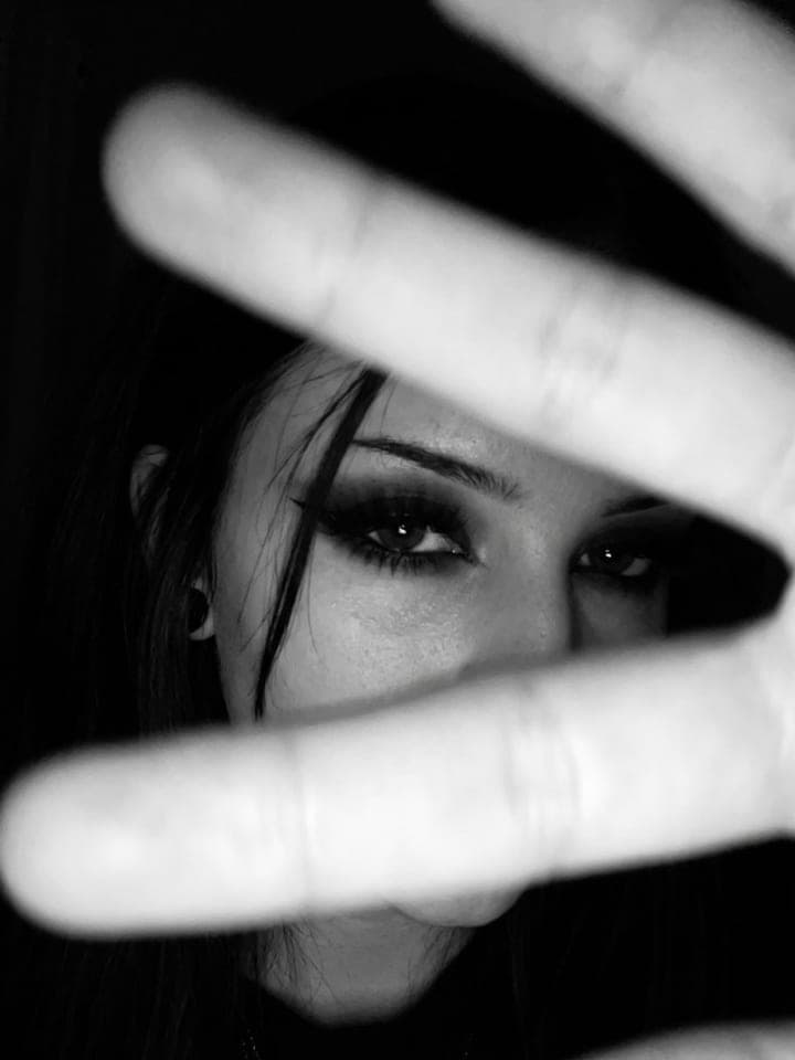 Black-and-white flash selfie of a dark-haired woman looking through fingers held close to the lens