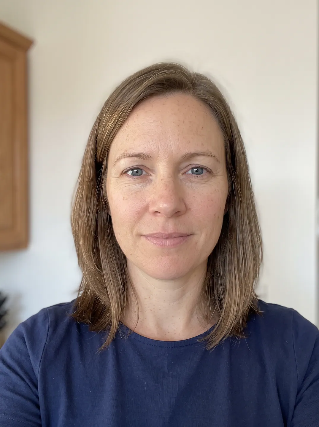 Selfie of a woman with straight light brown hair and blue eyes in a navy T-shirt, used as the input